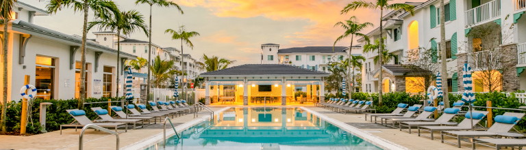 A beautiful pool surrounded by lounge chairs, palm trees and apartment buildings