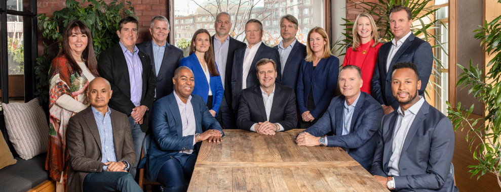 A group of people in office attire, surrounding a desk, posing for a photo