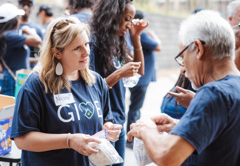 A woman talking to a man at a community event. Each person is wearing a GIVE shirt