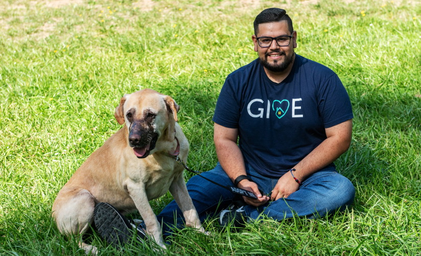 A man wearing a GIVE shirt sitting on grass with a dog