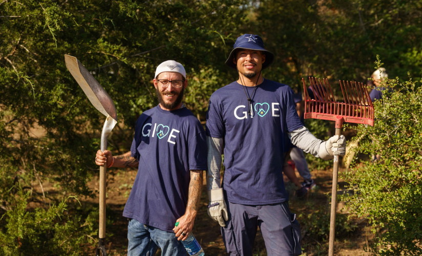 Two men wearing GIVE shirts and holding gardening tools