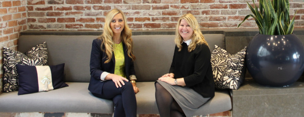 Two women smiling at the camera, sitting next to each other